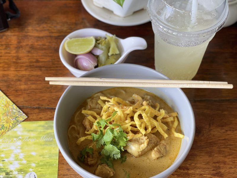 ข้าวซอยไก่หนึ่งชามกับถ้วยมะนาว หอมแดง และผักกาดดอง วางข้างน้ำมะนาวโซดา