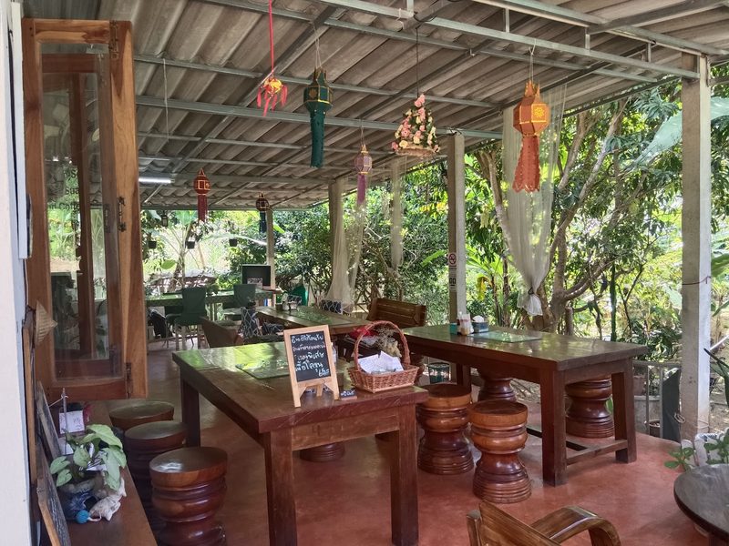 ลานนั่งกินใต้หลังคาโปร่ง มีโต๊ะไม้ยาวและเก้าอี้ตอไม้