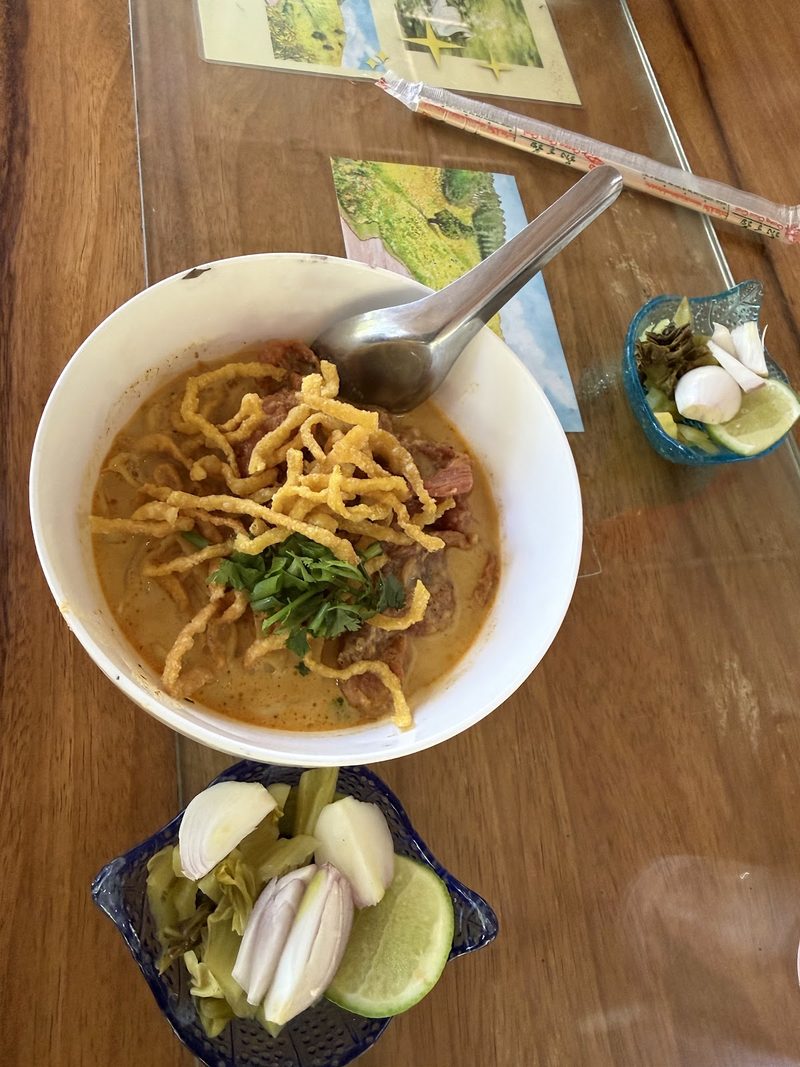 ข้าวซอยถ่ายจากด้านบน วางคู่ถ้วยเครื่องเคียงบนโต๊ะไม้