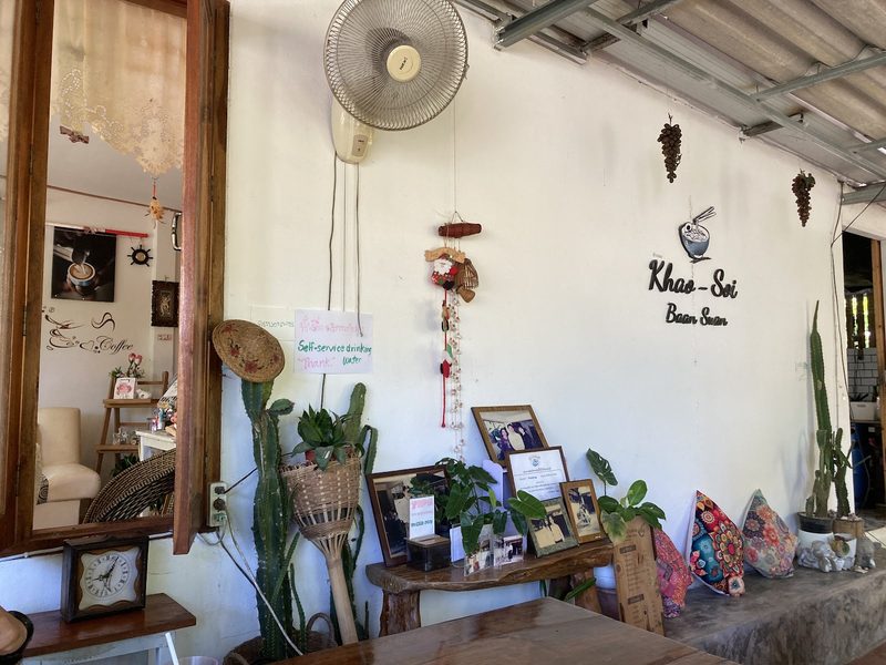 ผนังในร้านที่มีโลโก้ Khao-Soi Baan Suan หมอนอิงลายผ้า และกรอบรูป